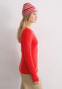 Rotes Langarmshirt aus weichem Stoff, kombiniert mit einer rot-weiß gestreiften Strickmütze. Das Shirt hat einen runden Halsausschnitt.