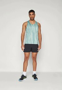 Világos türkiz színű ujjatlan felső, függőleges hullámos csíkokkal, fekete sportnadrággal párosítva. Kényelmes szabású és réteges textúrájú.