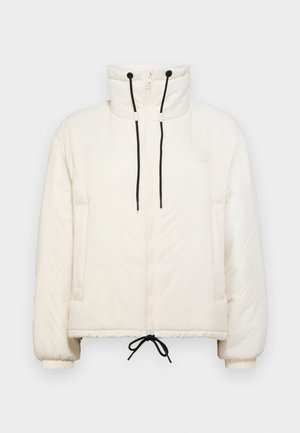 Chaqueta tipo plumón en color crema con cuello alto, cierre de cremallera, cordones negros y puños elásticos. Presenta bolsillos laterales y un corte rectángulo.