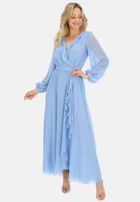 Jasnoniebieska sukienka maxi z falbaniastymi detalami, długimi przezroczystymi rękawami i paskiem w talii. Zwiewny materiał nadaje lekki ruch.
