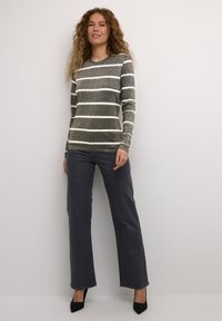 Maglietta a maniche lunghe a righe grigia con righe bianche, abbinata a jeans grigi scuri con leggere decorazioni, completata da tacchi neri.