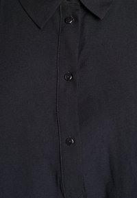 Schwarzes Hemd mit Knopfleiste, das einen Kragen und gleichmäßig verteilte schwarze Knöpfe an der Vorderseite aufweist, mit einer glatten Textur und strukturiertem Design.