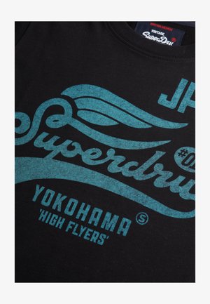 Sort bomulds T-shirt med turkise vintage grafiske tryk, inklusive ordene "Superdry," "Yokohama," og dekorative spiralmotiver.
