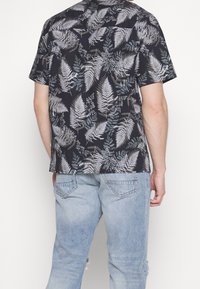 Zwart T-shirt met korte mouwen met een varen- en loofpatroon in tinten groen en grijs. Draag het met lichtblauwe versleten spijkerbroek.