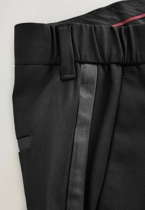 Schwarze Hose aus strukturiertem Stoff, mit elastischem Bund und einem eleganten, glänzenden Seitenstreifen. Enthält Seitentaschen und Gürtelschlaufen.