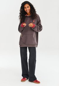 Šedá mikina s červenými akcentmi a predným vreckom, skombinovaná s čiernymi nohavicami širokého strihu a červenými topánkami. Obsahuje detail loga na hrudi.