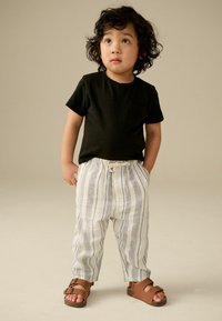 Schwarzes T-Shirt mit kurzen Ärmeln und Tasche, kombiniert mit weiß-grau gestreiften Hosen und braunen Schnallensandalen. Hat eine lockere Passform und leichten Stoff.