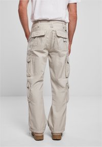 Pantalones cargo beige con múltiples bolsillos laterales y un corte relajado, fabricados con un tejido duradero de superficie ligeramente texturizada.