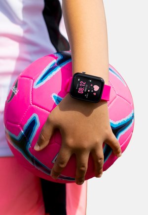 Montre intelligente noire avec un bracelet rose affichant l'heure et la date, tenue dans une main tenant un ballon de soccer rose avec des accents bleus et noirs.