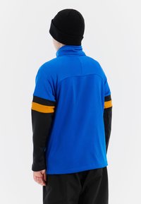 Niebieska sportowa koszulka z wysokim kołnierzem, czarnymi długimi rękawami i pomarańczowym paskiem; posiada siatkową strukturę w tylnym panelu.