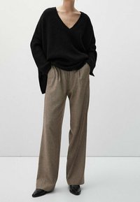 Black oversized knit sweater with a V-neck, paired with wide-leg beige plaid trousers, and black pointed-toe shoes. Smooth texture, casual fit.