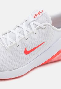 Chaussure de sport Nike avec une tige en mesh blanc, surface texturée, accents roses et une semelle rembourrée. Présente un logo swoosh reconnaissable.