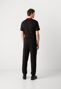 Zwarte katoenen shirt met korte mouwen en een rode halsafwerking, gecombineerd met zwarte sweatpants met een elastische tailleband en taps toelopende boorden.