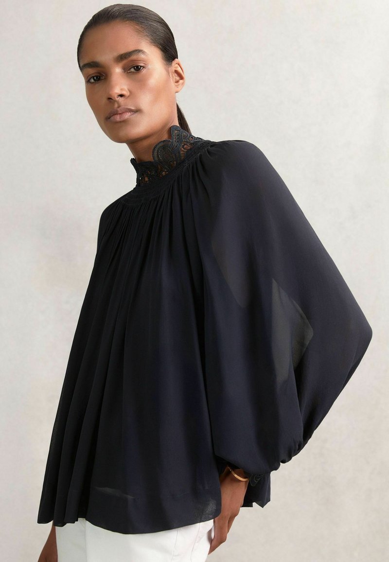 Schwarze, transparente Bluse mit hohem Spitzenkragen, gerafftem Oberteil und fließenden Fledermausärmeln, die über plissierte Details am Saum verfügt.