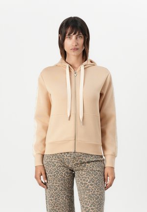 Light beige zip-up hoodie with drawstrings, featuring a smooth texture and ribbed cuffs, paired with leopard print pants.