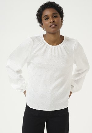 Witte blouse met lange mouwen, een getextureerd bloemenpatroon, een geplooide halslijn en elastische manchetten, gecombineerd met zwarte jeans.
