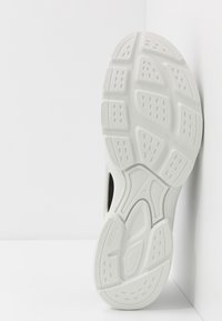 Valkoinen tennaripohja, jossa on kuvioituja tekstuureja ja reikiä. Koverat ja kuperat muotoilut parantavat pitoa ja joustavuutta. Selkeä merkintä ja koko 42.