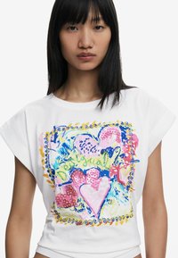 Weißes Baumwoll-T-Shirt mit einem bunten grafischen Design, das Herzen in Rosa, Blau und Grün zeigt, umrandet von einem dekorativen Muster.