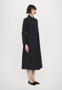Pikk tumesinine kaftan, mis on valmistatud siledast kangast, kahekordse nupuga, vöödiga talje ja klassikalise kraega.