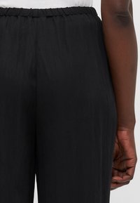 Mustat kevyet housut, joissa on joustava vyötärö, smooth pinnan ja rento istuvuus. Suunnittelussa on sivusaumat ja ei näkyviä taskuja.