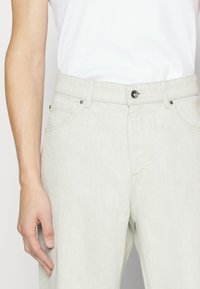 Pantalones de mezclilla gris claro con corte recto, que cuentan con bolsillos frontales, una bragueta visible y un cierre de botón de metal. Textura suave en toda la prenda.