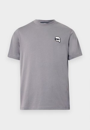 Maglietta in cotone grigia con colletto rotondo e maniche corte. Presenta un logo in bianco e nero cucito sul lato sinistro del petto. Design liscio e informale.