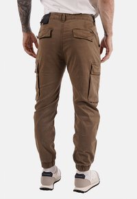 Pantaloni cargo marroni con polsini elasticizzati, multiple tasche laterali, una texture liscia e una vestibilità comoda e rilassata, progettati per comfort e funzionalità.