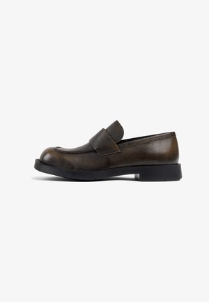 Mocasín de cuero marrón con punta redonda, suela plana de goma negra y una correa ancha en la parte superior para un ajuste seguro.