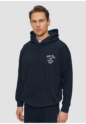 Granatowy hoodie wykonany z mieszanki bawełny, z kieszenią z przodu i haftem "Slow Pace Running Club" na klatce piersiowej. Przytulny i luźny krój.