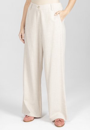 Beżowe spodnie o szerokich nogawkach z bocznymi kieszeniami, noszone z różowymi mokasynami z frędzlami, pokazane od talii do stóp na neutralnym tle.