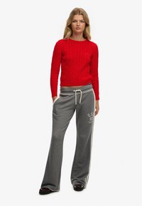 Rød kabelstrikket sweater og grå sweatpants med sidestreger og logodetaljer, kombineret med mørke sko. Simpelt afslappet outfit.