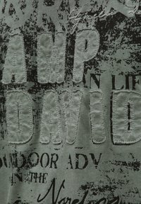 Green fabric with stitched large letters "CAMP DAVID" and black printed partial text with distressed design.