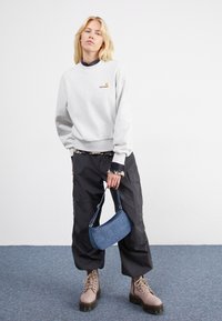 Szary sweatshirt z małym logo, czarne spodnie cargo, beżowe buty na sznurówki oraz niebieska torebka dżinsowa. Ustawione na jednolitym tle.