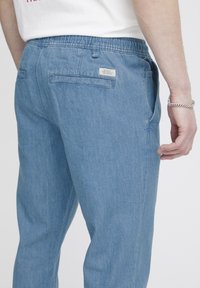 Pantalones de mezclilla azul claro con cintura elástica, que cuentan con dos bolsillos traseros y una pequeña etiqueta cosida en el bolsillo derecho.