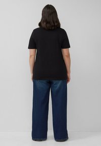 Zwarte katoenen T-shirt met korte mouwen, gecombineerd met brede blauwe denim broeken. De outfit heeft een ontspannen pasvorm en een minimalistisch ontwerp.