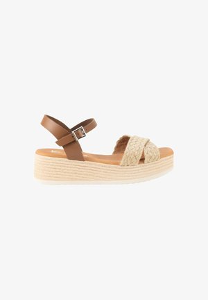 Sandalia de cuña con tiras delanteras trenzadas en beige, correa marrón en el tobillo con hebilla plateada y suela de plataforma texturizada en beige claro.