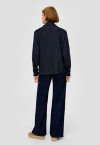 Marine ribbeltrui met hoge kraag, gecombineerd met wijde, donkere jeans en beige plateau schoenen. Soepele textuur en ontspannen pasvorm.