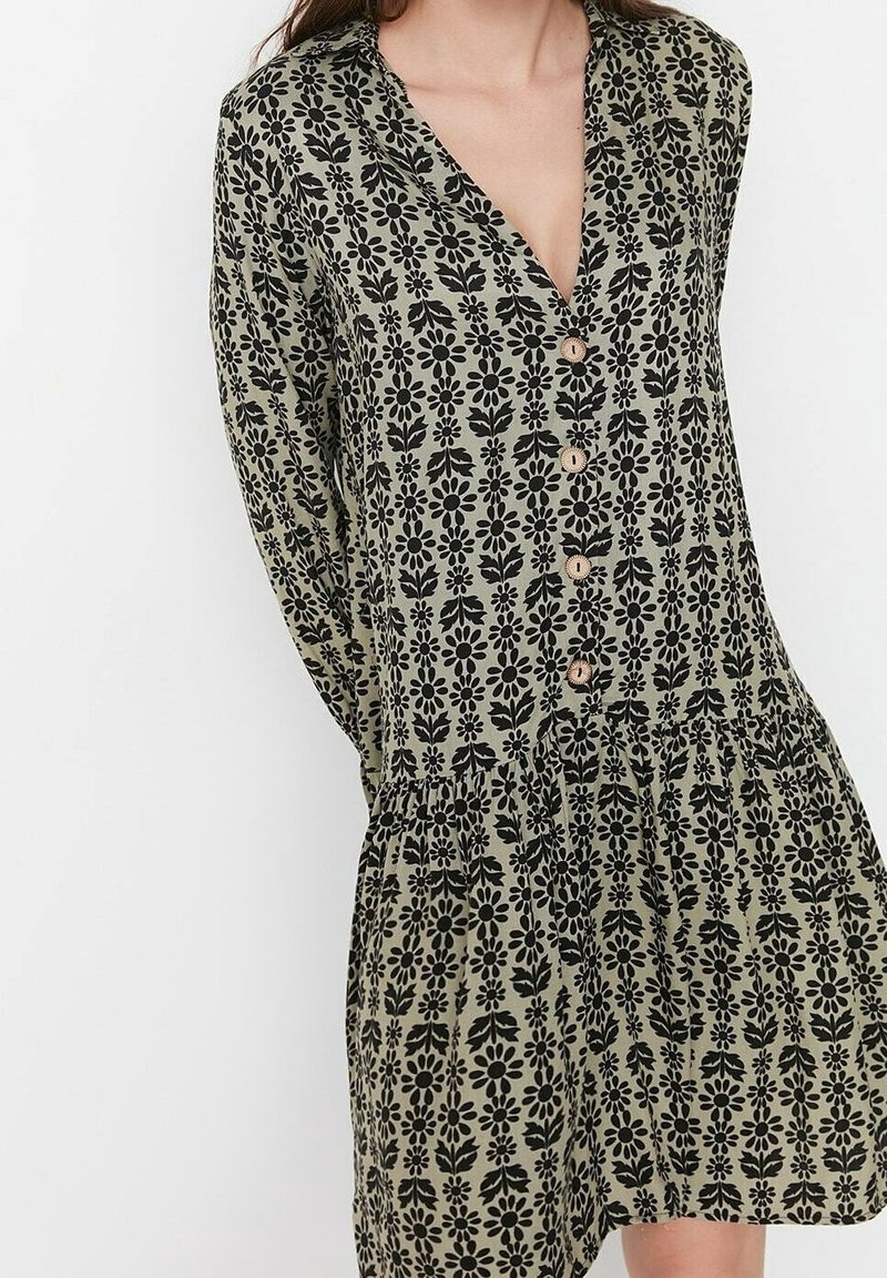 Blommönstrad klänning i olivgrön med svarta blommor. V-ringning, knappstängning fram, lång ärm och rynkad midja.