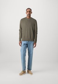 Suéter verde oliva con cuello redondo y dobladillo acanalado, combinado con jeans de corte relajado en azul claro y zapatos planos beige.