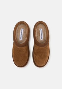 Brown suede slippers with a soft, plush lining and elasticated collar. Features a subtle logo tag and rounded toe design.