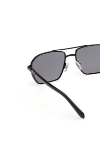 Gafas de sol con montura de metal negro y lentes rectangulares tintados oscuros, con almohadillas nasales ajustables y transparentes sobre un fondo blanco.