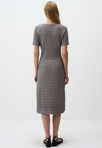 Robe midi en tissu à motifs, avec des manches courtes, une coupe cintrée et un col rond, accompagnée de sandales plates noires.