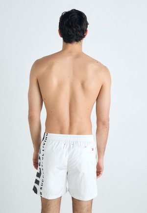 Shorts de bain blancs avec un graphisme noir sur le côté, ceinture élastique et une poche arrière. Texture lisse, design moderne avec un minimum de détails.
