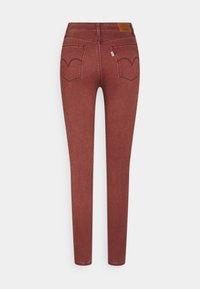 Jean marron taille haute et coupe slim avec deux poches arrière et coutures décoratives sur un fond uni.