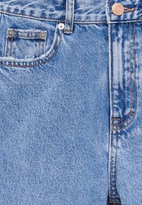 Light blue denim jeans featuring a faded texture, five-pocket design, and silver hardware accents, including a button and rivets.