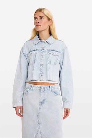 Világoskék farmer cropped dzseki gombos elülső részével, két mellzsebbel és megviselt szegéllyel, egy hozzá illő világoskék farmer szoknyával párosítva.