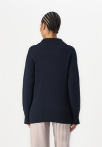 Navy blue knitted sweater with a shawl collar, relaxed fit, and ribbed cuffs, paired with light ribbed pants. No visible patterns or hardware.