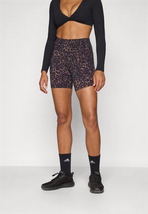 Shorts s uzorkom leoparda visokog struka od glatkog materijala, upareni s crnim atletskim cipelama i čarapama s logotipom.