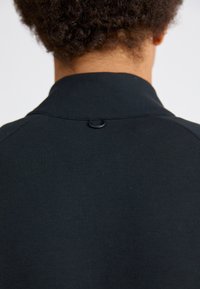 Sudadera negra con una textura suave, un cuello elevado y un pequeño detalle de lazo en la parte posterior. Material de mezcla de algodón.