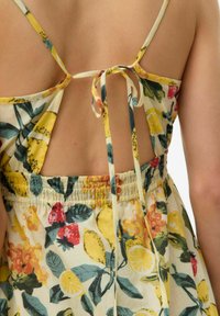 Robe fleurie avec des motifs jaunes, verts et rouges ; présente des bretelles spaghetti et un dos noué. Le tissu est léger et texturé.